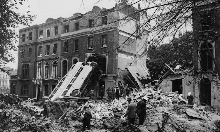 A bus leans against the debris from bombed houses
