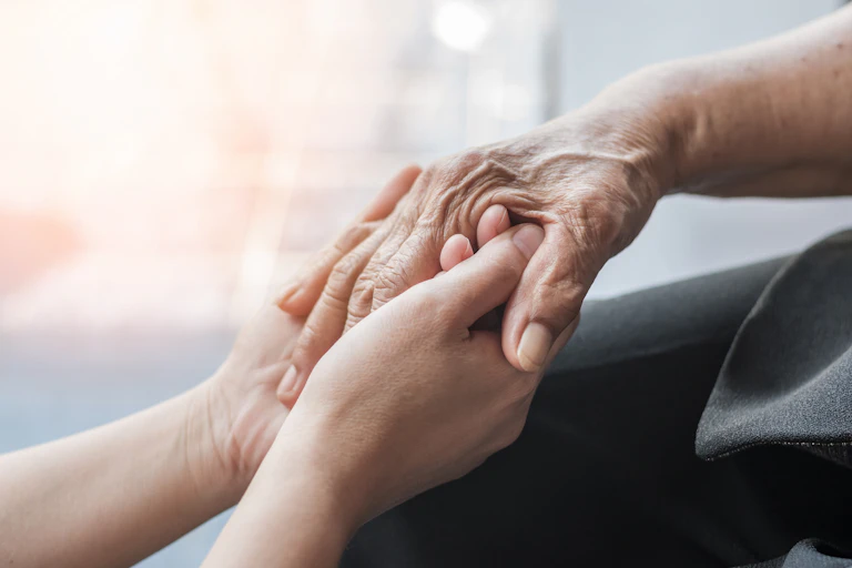 The hands of a nurse clasping the hand of a patient in a show of comfort and support.