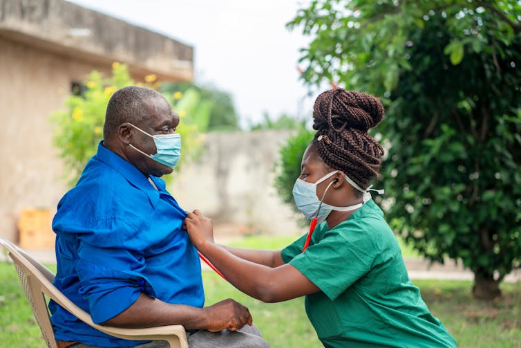 Young healthworker attending an elderly person outside in a garden during COVID-19.