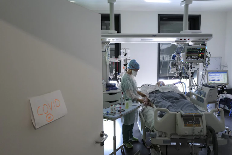 Personne allongée sur un lit de réanimation, avec une soignante à son chevet.