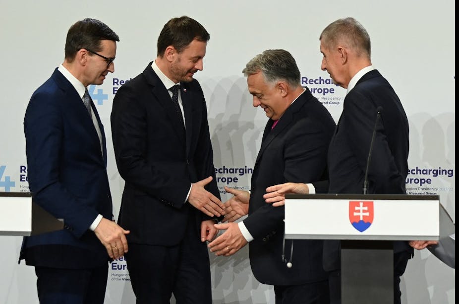 4 hommes en costumes se serrent la main en souriant.