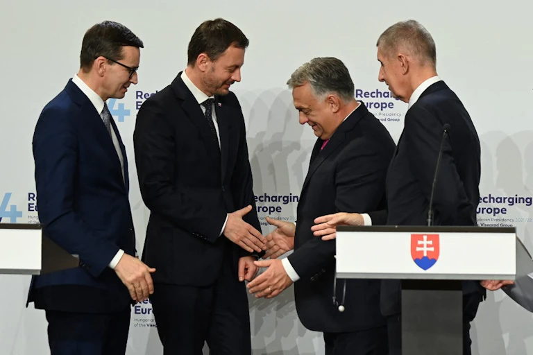 4 hommes en costumes se serrent la main en souriant.