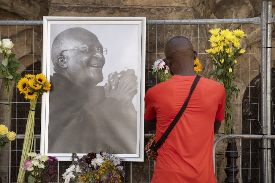 Un homme se recueille devant une photo en noir et blanc de Desmond Tutu.