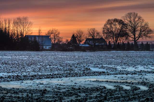 Sunrise above a house and snowy field.