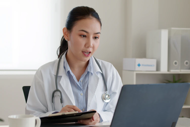 A doctor sitting at her desk teleconferencing on her laptop