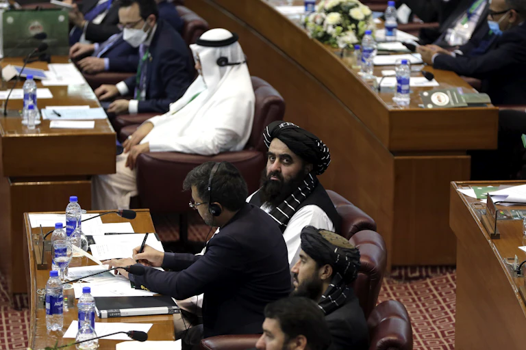 A bearded man wearing a black head scarf looks at the camera at a meeting.