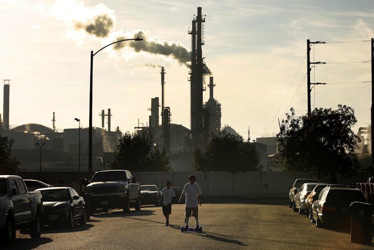 Kids on skateboards with refinery behind them.