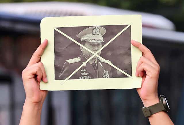 Two hands hold up a photo of a general in a military uniform with an X over his face.