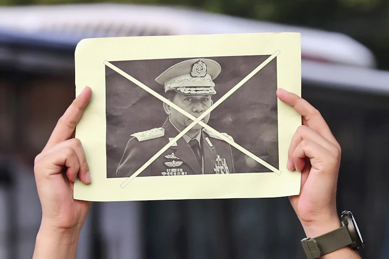 Two hands hold up a photo of a general in a military uniform with an X over his face.