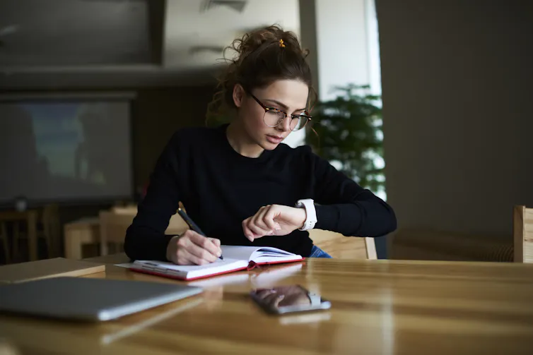 A woman writes in a journal while looking at her watch