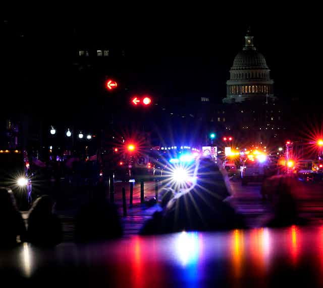 Silhouetted figures are seen against police lights and the U.S. Capitol building at night.