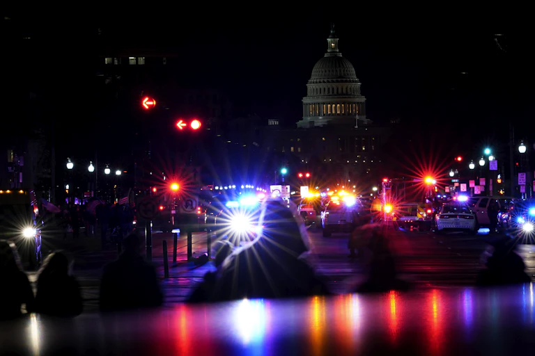 Silhouetted figures are seen against police lights and the U.S. Capitol building at night.