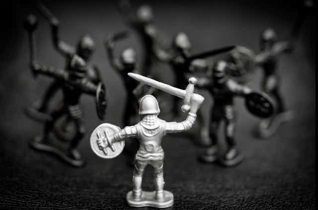 A black and white photo of toy knights in battle, one white and the remainder darker and out of focus