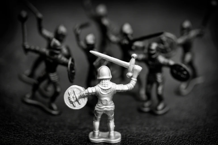 A black and white photo of toy knights in battle, one white and the remainder darker and out of focus