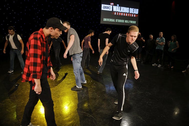 People are seen rehearsing a zombie scene, staggering.