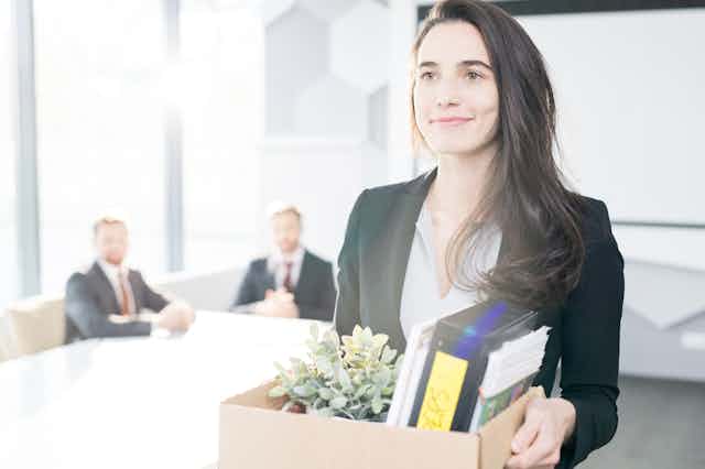 Woman leaves office smiling holding a box of her things