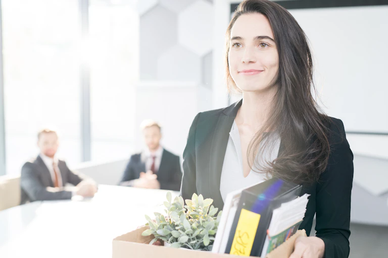 Woman leaves office smiling holding a box of her things