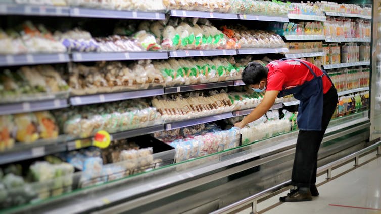 A man bends over, stocking shelves, in a fridge aisle at the grocery store.