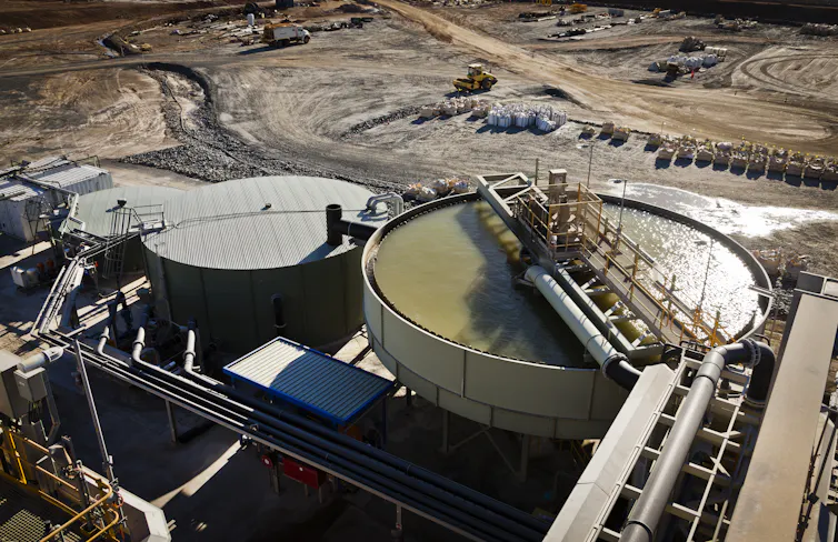 Large outdoor tanks, one filled with a greenish fluid, at a mineral processing plant.