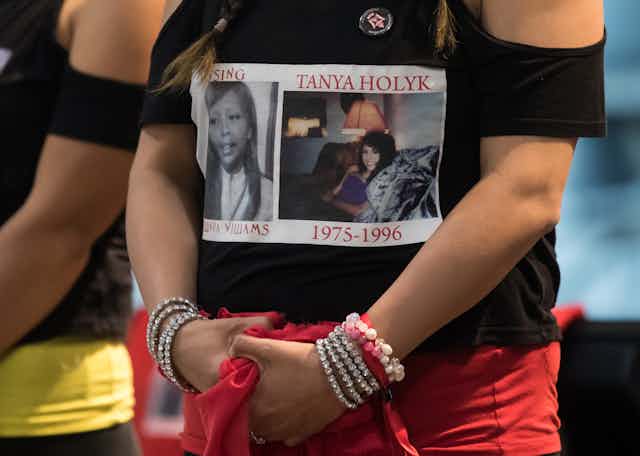 A woman stands, on her shirt is a photo labelled 'Tanya Holyk 1975-1996' and 'Missing Belinda Williams'
