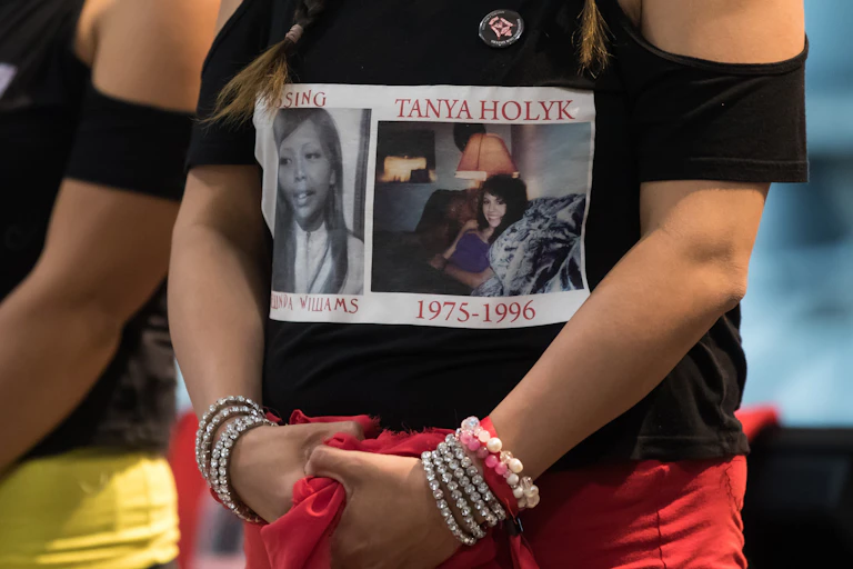 A woman stands, on her shirt is a photo labelled 'Tanya Holyk 1975-1996' and 'Missing Belinda Williams'