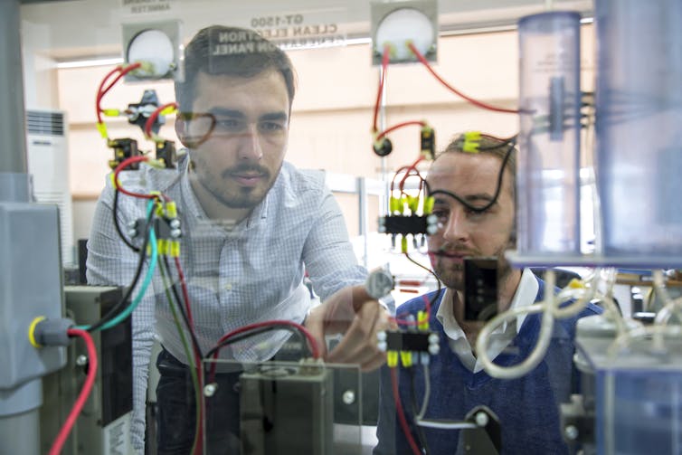 Two engineers shown through a window work on a renewable energy project with wires