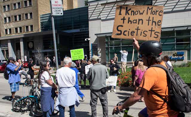A protestor outside a hospital holds a sign that says 'I know more than the scientists.'
