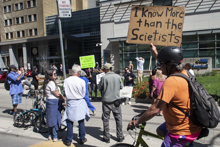 A protestor outside a hospital holds a sign that says 'I know more than the scientists.'