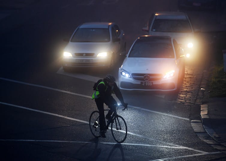 A person rides in the fog past some cars.