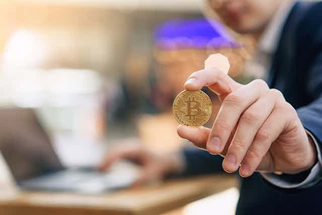 Una mano sujeta una moneda de bitcoin con el índice y el pulgar.