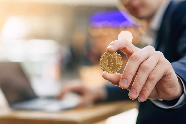 Una mano sujeta una moneda de bitcoin con el índice y el pulgar.