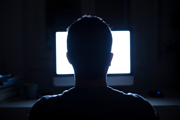 The back of a person's head looking at a computer screen in the dark.