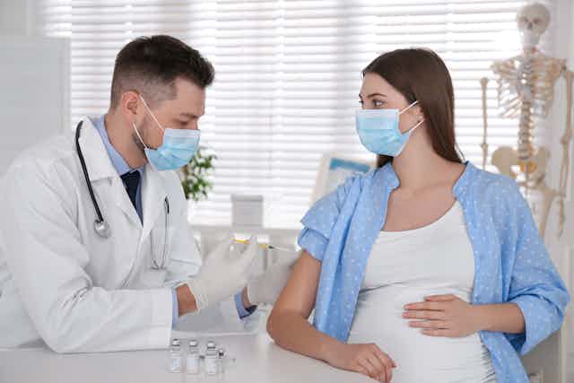 un médico con mascarilla vacuna a una mujer embarazada con mascarilla