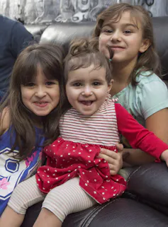 Three young girls, on a toddler, smile as their father sits behind them on a leather couch.