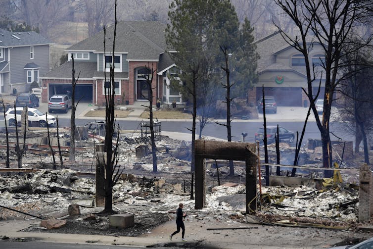 A runner passes the outlines of burned homes, with unburned houses behind them