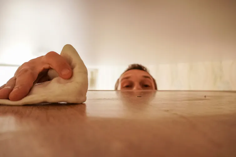 A man dusts on top of a shelf.