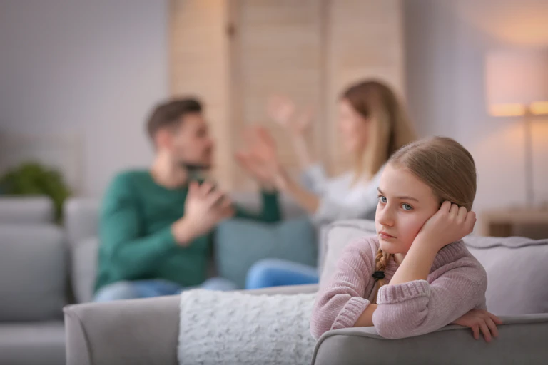 Child resting head in hand while parents argue in background