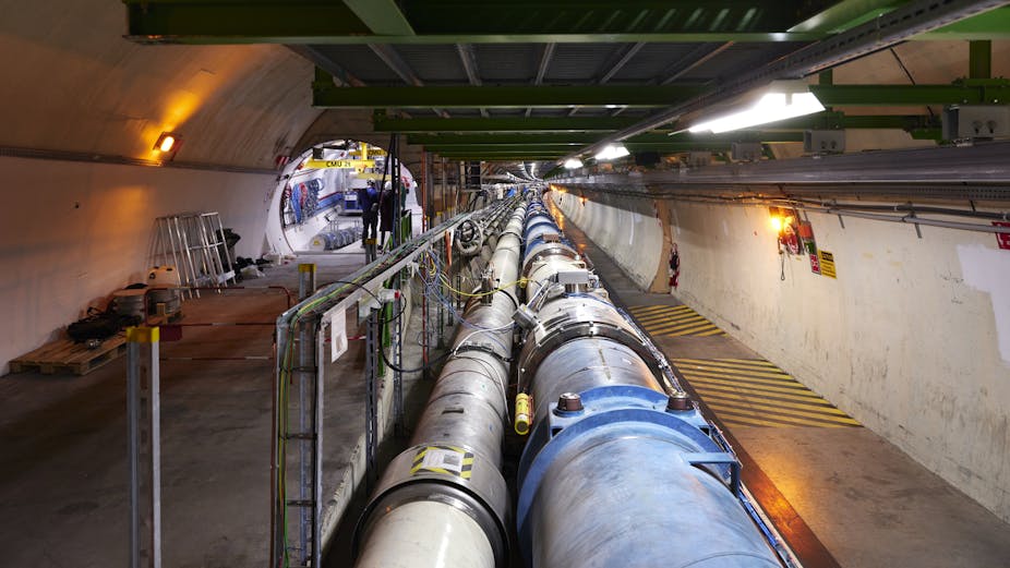 Tuyaux formant l'anneau du LHC, un tunnel s'ouvre à leur gauche, avec un autre instrument en cours d'installation.