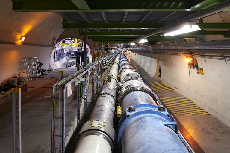 Tuyaux formant l'anneau du LHC, un tunnel s'ouvre à leur gauche, avec un autre instrument en cours d'installation.