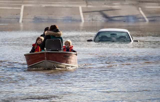 A woman and two children in a boat with a submerged car behind them.