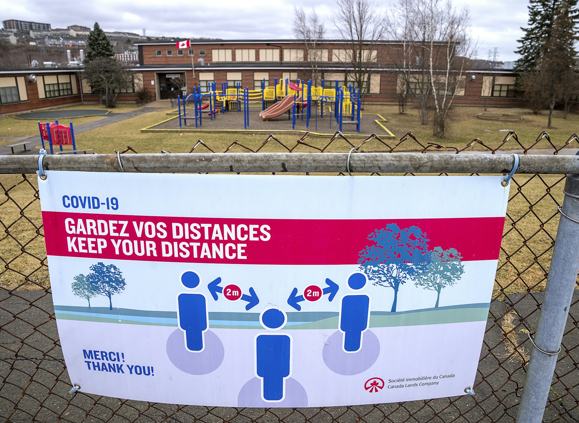 A sign reads 'gardez vos distances' or 'keep your distance' on the fence of a school yard.