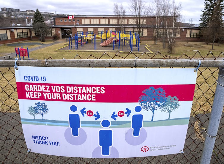A sign reads 'gardez vos distances' or 'keep your distance' on the fence of a school yard.