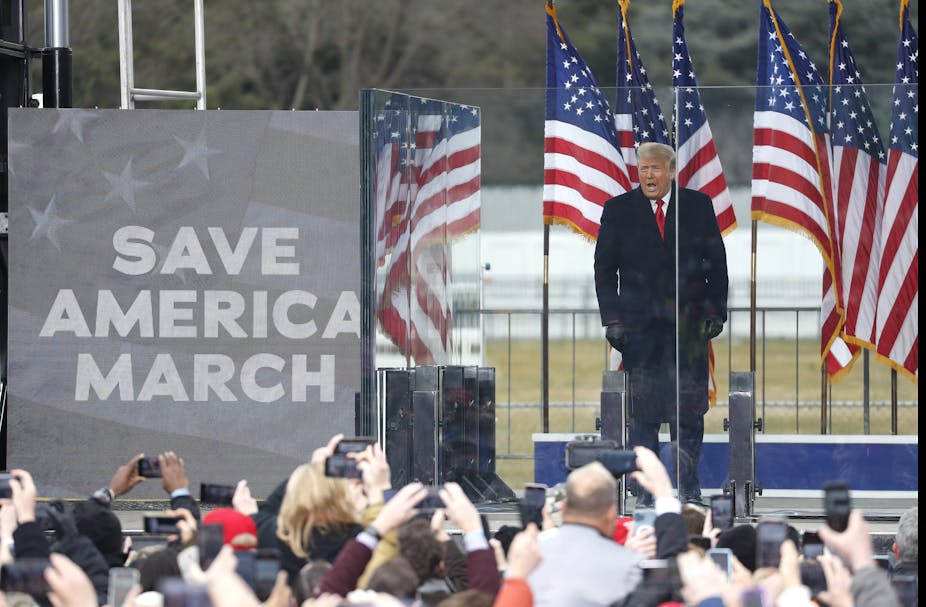 Donald Trump speaking to a crowd of his supporters in Washington DC on January 6 2021 with a Save America March placard in trhe foreground and US flags in the background..