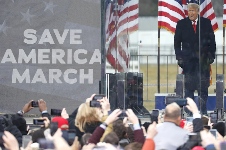 Donald Trump speaking to a crowd of his supporters in Washington DC on January 6 2021 with a Save America March placard in trhe foreground and US flags in the background..