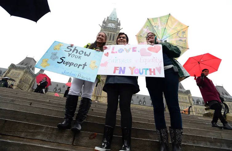 Trois femmes se tiennent ensemble et tiennent des pancartes sur lesquelles on peut lire « montrez votre soutien » et « aimez les jeunes des Premières nations »