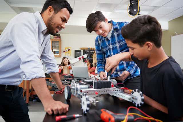 Un enseignant aide deux élèves à construire un robot.
