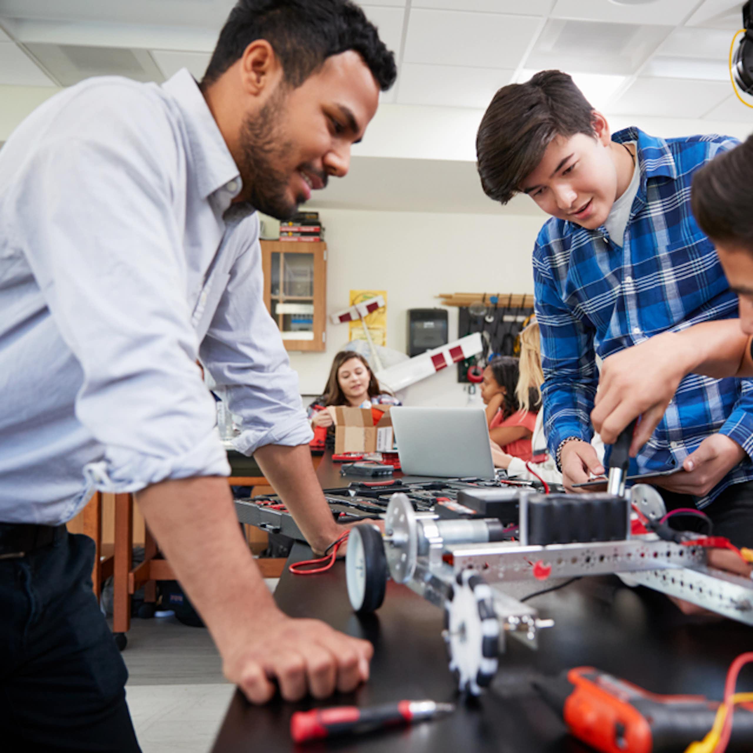Un enseignant aide deux élèves à construire un robot.