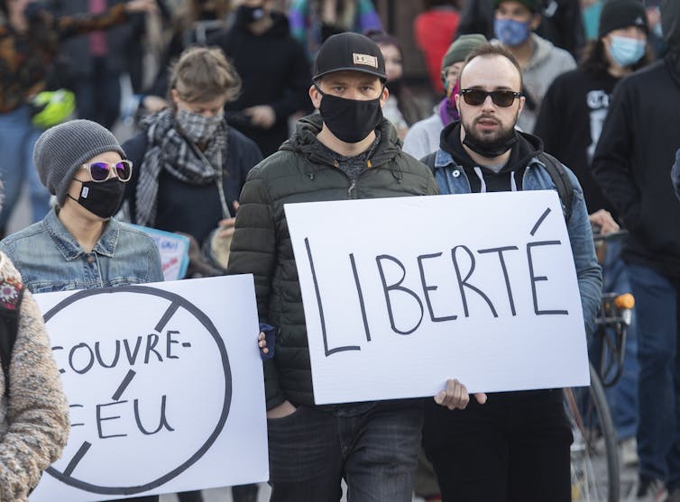 People wear maskes and march, holding signs that read 'liberté' and 'no couvre-feu'