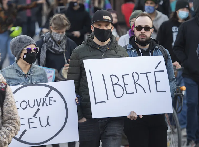 People wear maskes and march, holding signs that read 'liberté' and 'no couvre-feu'