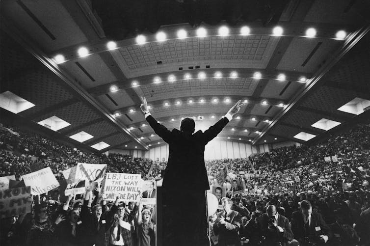 Richard Nixon, con un traje oscuro y mostrando una 